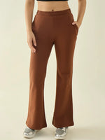 Woman in 98degreenorth Rust Flared Bootcut Trousers, black crop top, and silver sneakers stands hands in pockets.