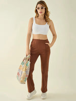 Woman in a white crop top, 98degreenorth rust straight fit trousers, white sneakers, sunglasses, and a striped tote.