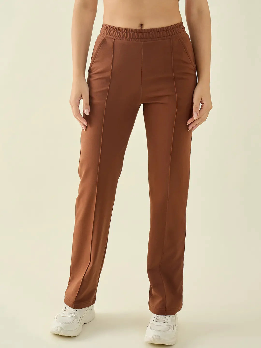 Woman in 98degreenorth Rust Straight Fit Cotton Stretchable Trousers, styled with white sneakers against a beige backdrop.