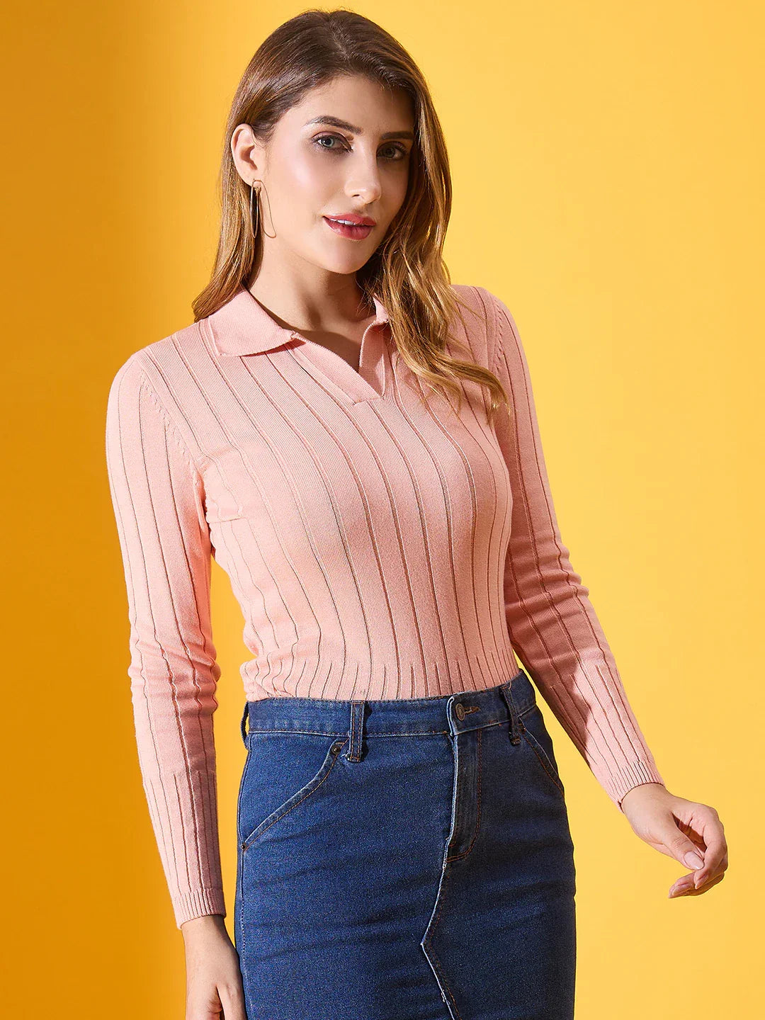Woman wears 98degreenorth’s salmon ribbed collar neck sweater and denim skirt against a bright yellow background.