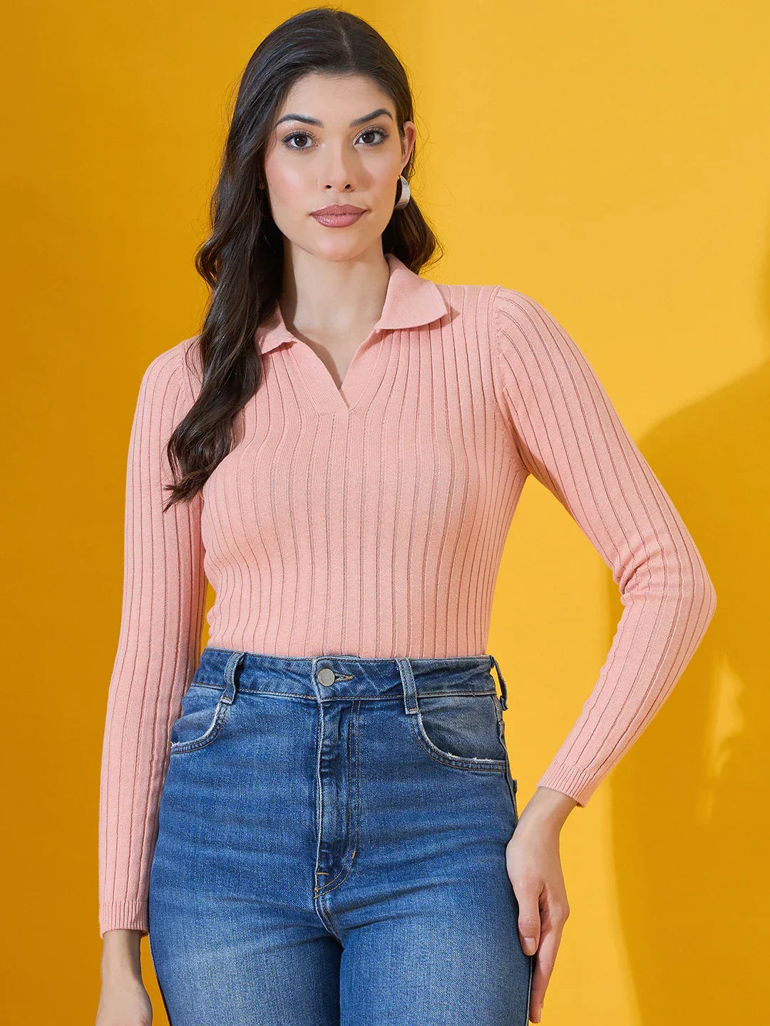 Woman in 98degreenorth’s Salmon Ribbed Collar Neck Sweater and blue jeans stands against a yellow background.