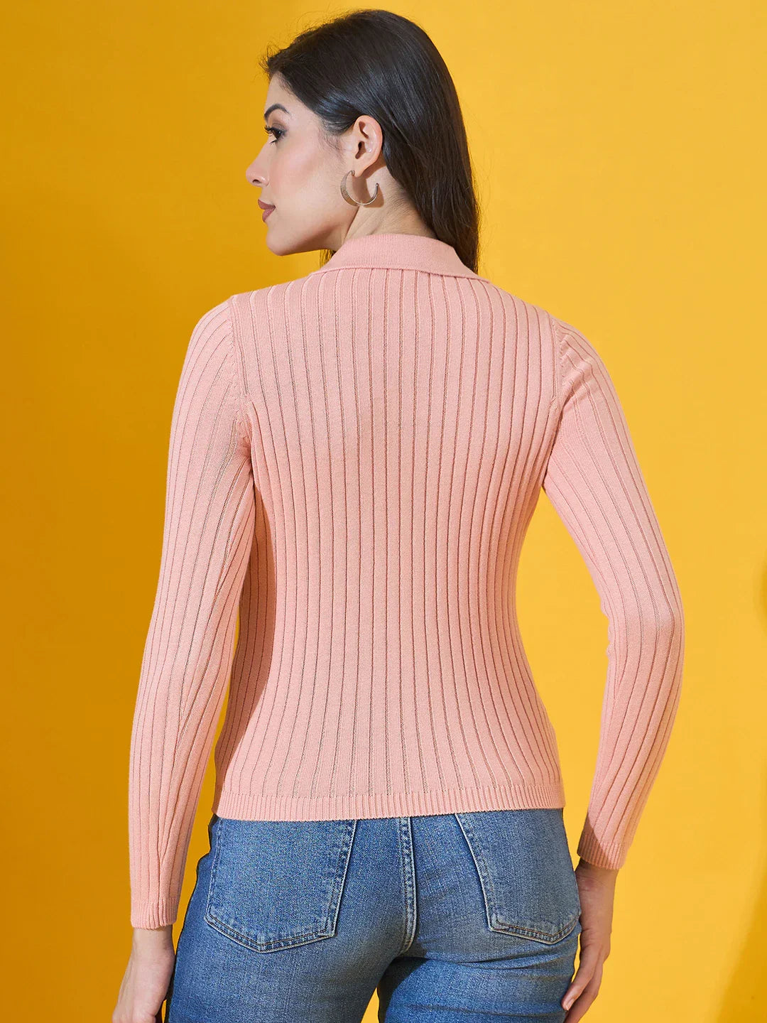 Woman in a 98degreenorth salmon ribbed collar neck sweater and blue jeans, facing away, yellow background.