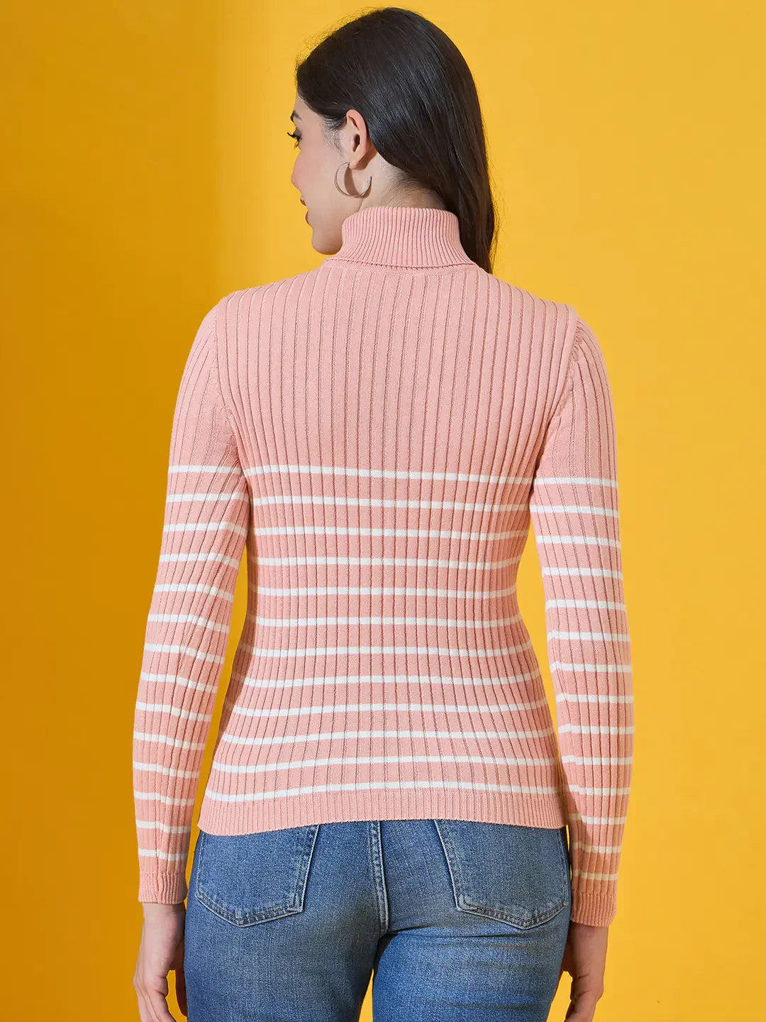 Woman in a 98degreenorth salmon ribbed turtleneck sweater and jeans, facing away on a yellow background.