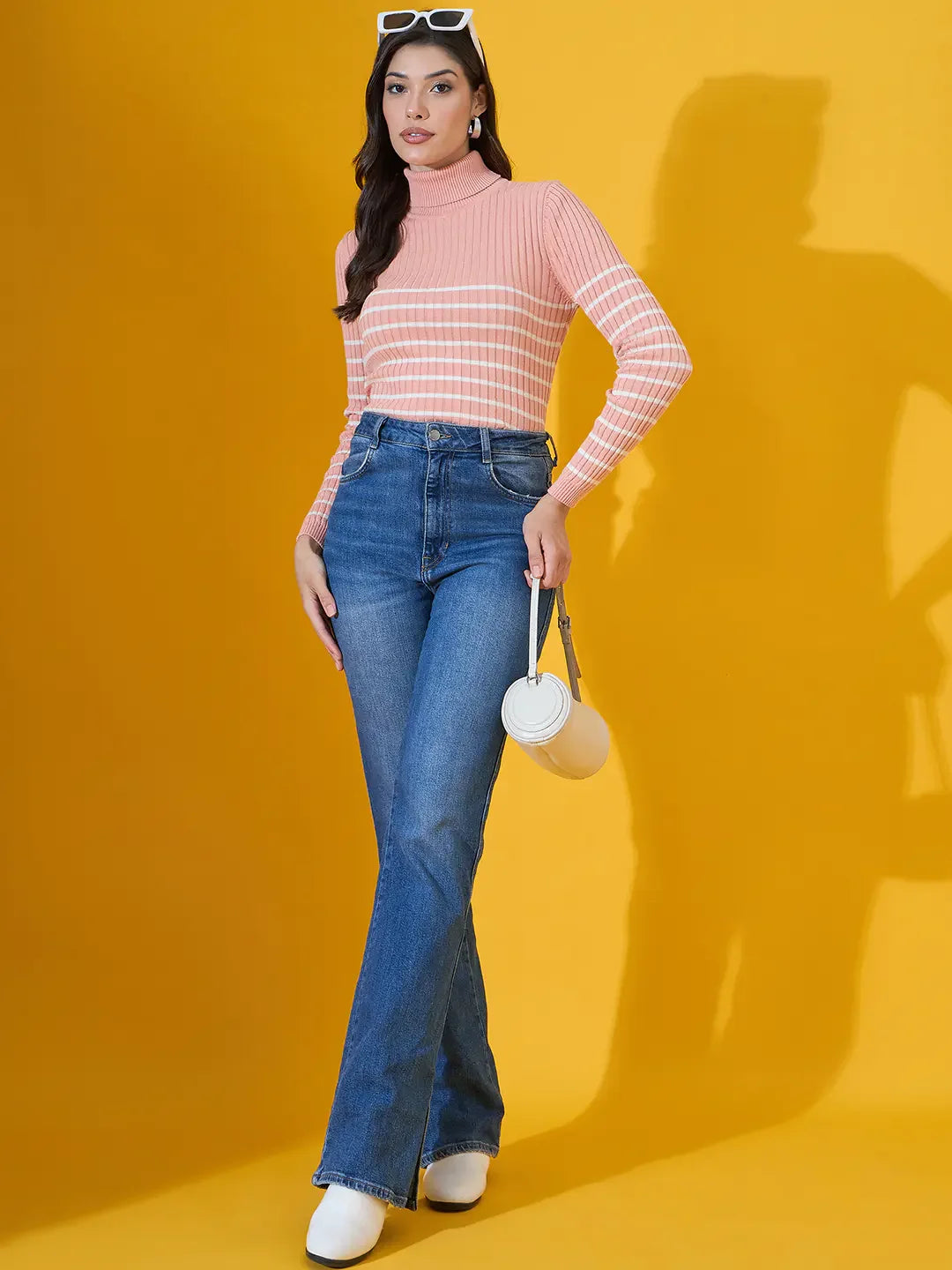 Woman in a 98degreenorth salmon ribbed turtleneck sweater, blue jeans, white shoes, sunglasses, and a small white purse.