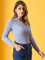 Woman in a 98degreenorth sky blue ribbed collar sweater and jeans, standing against a yellow background.