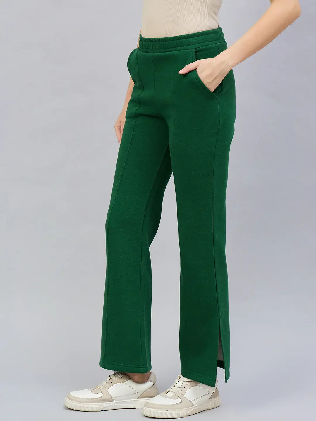 Model in 98degreenorth Women’s Smiley Green Flared Bootcut Sweatpants with side slit, beige top, and white sneakers.