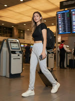 A woman in 98degreenorth Women's Straight Fit Cotton Trackpants in Light Grey walks through an airport.