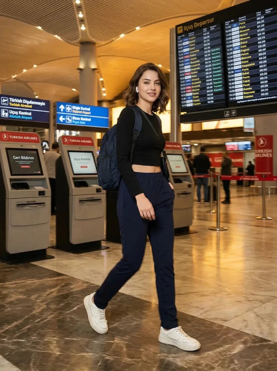 A woman wearing 98degreenorth Women's Straight Fit Cotton Trackpants in Navy smiles while walking through an airport.
