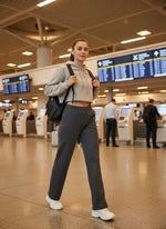 A woman in 98degreenorth Women’s Straight Fit Fleece Sweatpants in Anthra walks past airport flight info boards.