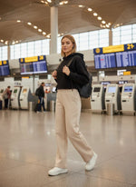 Woman in a black hoodie and 98degreenorth beige fleece sweatpants stands with a backpack near airport self-check-in kiosks.
