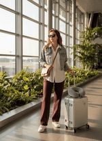 A woman in 98degreenorth Women’s Straight Fit Fleece Sweatpants in Dark Wine enjoys warmth at a bright airport terminal.