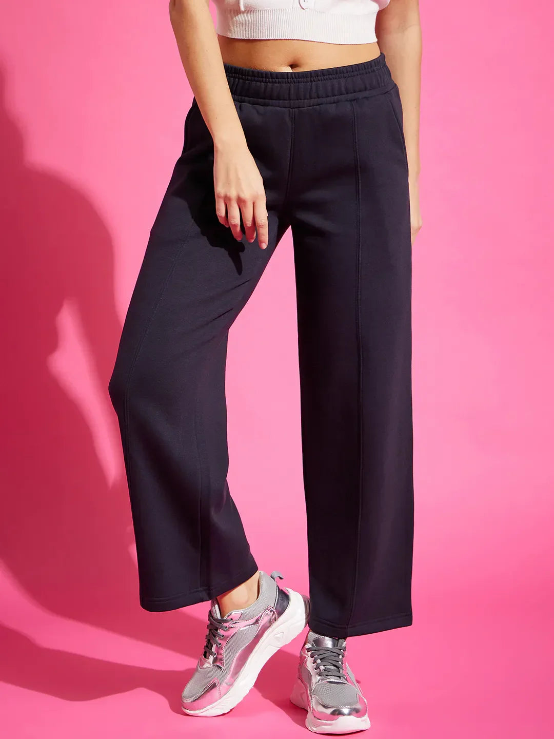A person in 98degreenorth Women’s Straight Fit Fleece Sweatpants in Navy and a white crop top stands against a pink background.