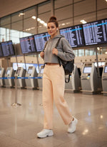 A woman in 98degreenorth Women’s Straight Fit Fleece Sweatpants in Peach stands near airport check-in kiosks.