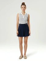 A woman in a 98degreenorth Women's Striped Knit Polo Vest pairs preppy-chic with a navy pleated skirt on white backdrop.