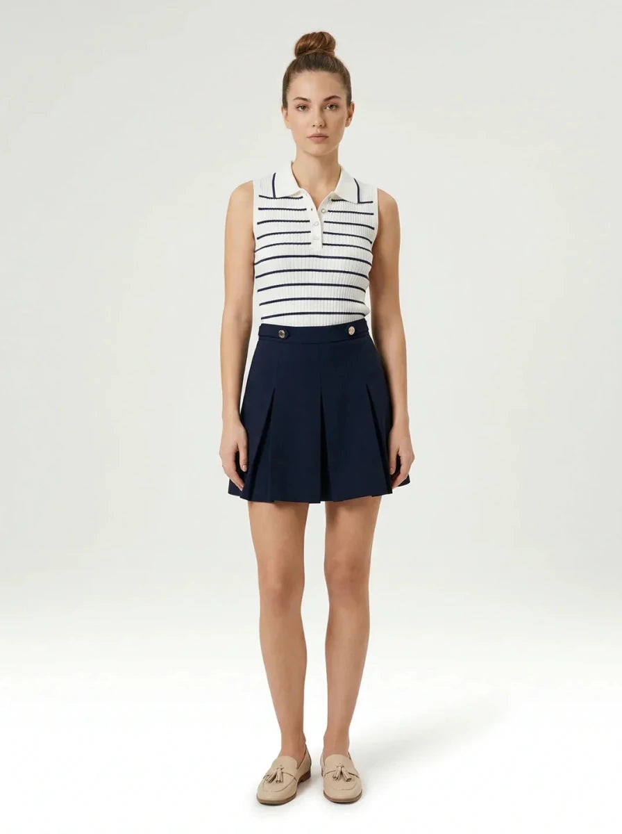 A woman in a 98degreenorth Women's Striped Knit Polo Vest pairs preppy-chic with a navy pleated skirt on white backdrop.