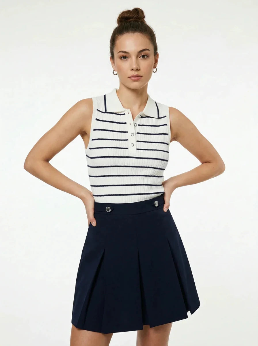 She wears the 98degreenorth Women's Striped Knit Polo Vest - White & Navy, styled with a navy pleated skirt.