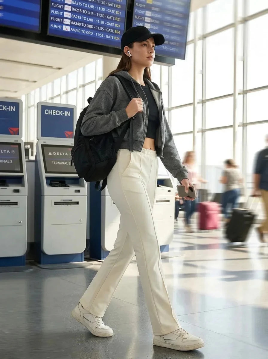 A woman in 98degreenorth Women's Tailored Straight Leg Pants in Butter walks near Delta airport check-in kiosks.