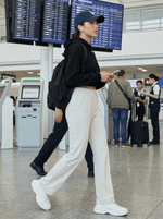 A woman in 98degreenorth Women's Tailored Straight Leg Pants in Ecru checks her phone at the airport.