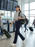 Woman wearing 98degreenorth Women's Navy Tailored Straight Leg Pants strolls through airport with luggage.