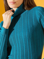 A woman models the 98degreenorth teal blue ribbed turtleneck sweater, perfect winter wear in India, against a yellow backdrop.