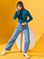 Woman models 98degreenorth’s teal blue ribbed turtleneck sweater against a bright yellow background.