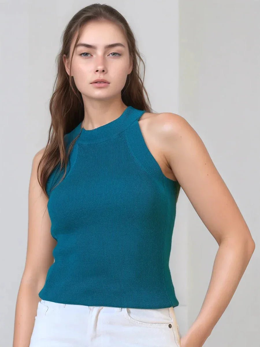 Woman with long brown hair wears 98degreenorth’s Teal Ribbed Halter Neck Sleeveless Knit Top and white pants.