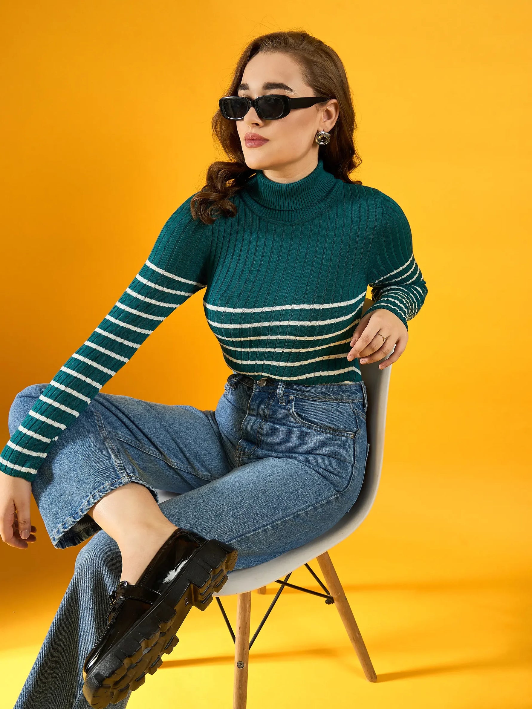 Woman in 98degreenorth’s teal ribbed knit turtleneck sweater sits against a bright yellow background.