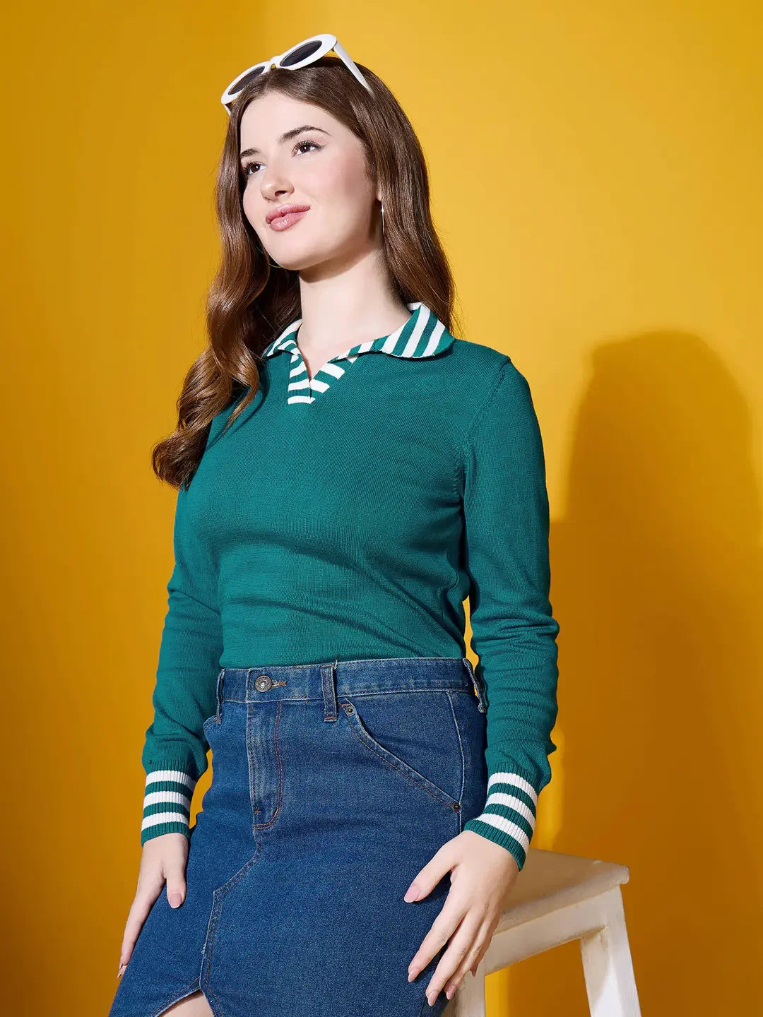 Woman in 98degreenorth’s teal striped collar knit sweater sits on a stool against a bright yellow background.