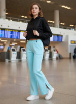 A woman in 98degreenorth’s turquoise bootcut fleece lounge pants stands in an airport terminal with a backpack.