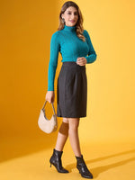 A woman in a 98degreenorth turquoise ribbed turtleneck sweater poses with a beige handbag against a yellow background.