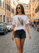 Woman in sunglasses wears a 98degreenorth Women’s Typography Cotton T-shirt on a city street with cars and colorful buildings.
