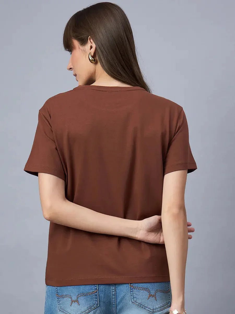Woman facing away in a 98degreenorth Women’s Typography Graphic Cotton T-shirt and blue jeans, on gray background.