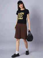 Woman in a 98degreenorth typography print cotton t-shirt, brown shorts, loafers, and black cap, holding a bag.