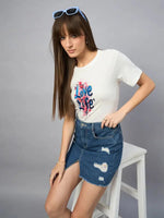 Woman in a 98degreenorth Women’s Typography Printed Cotton T-shirt and ripped denim skirt sits on a white stool.