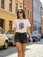 A woman in sunglasses and a 98degreenorth Women’s Typography Printed Cotton T-shirt walks past vintage cars.