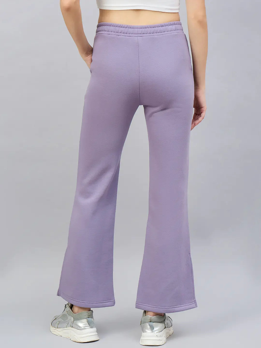 A person wears 98degreenorth Women’s Violet Flared Bootcut Sweatpants with side slit, seen from the back on a gray background.