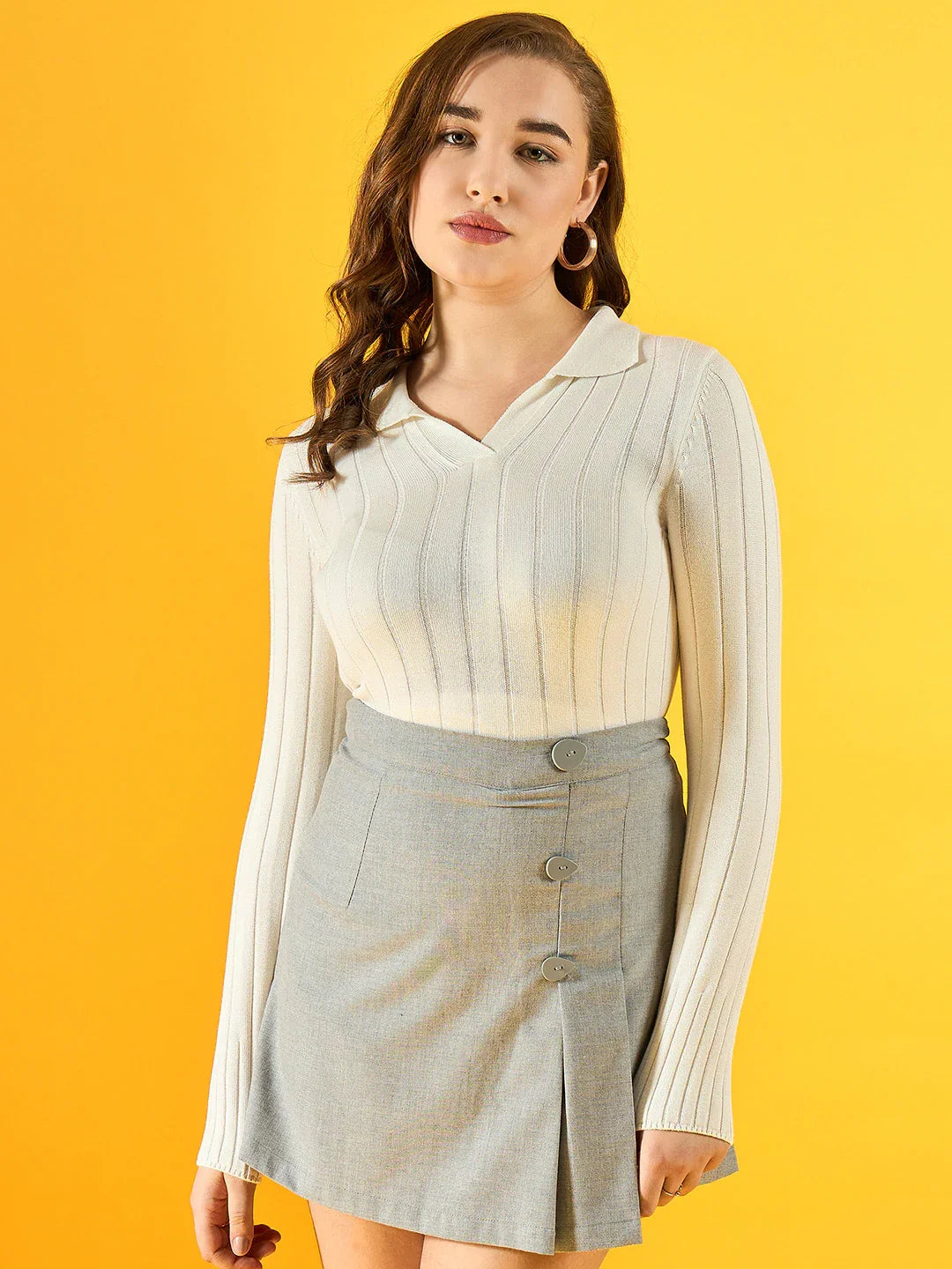 A woman in a 98degreenorth Women’s White Ribbed Collar Sweater poses against a yellow background in a gray skirt.