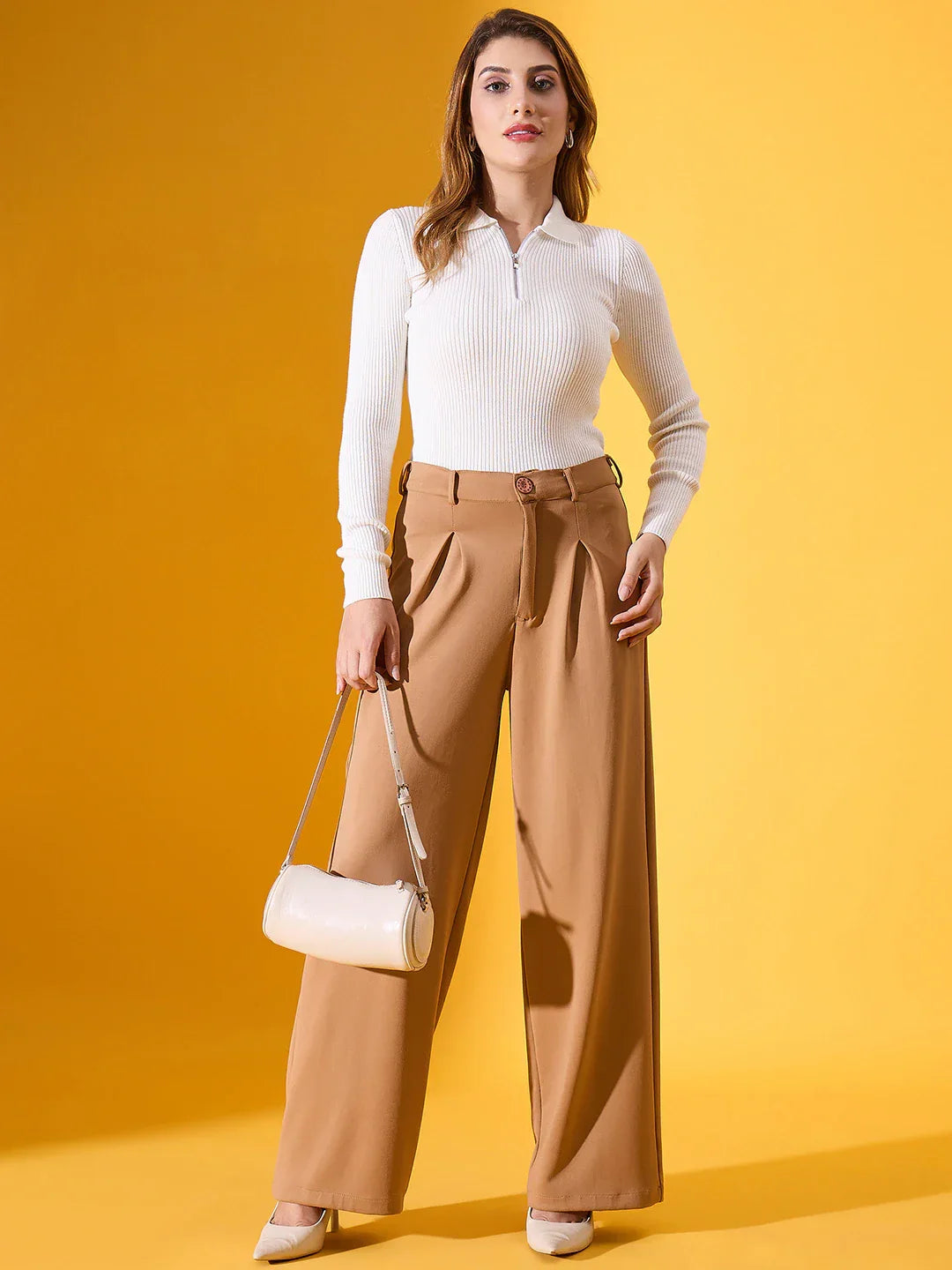 A woman wears 98degreenorth's white ribbed collar zipper sweater with tan pants, holding a cream bag on yellow backdrop.
