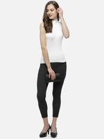 Woman in a 98degreenorth white ribbed high neck sleeveless knit top, dark pants, black heels, clutch, smiling.