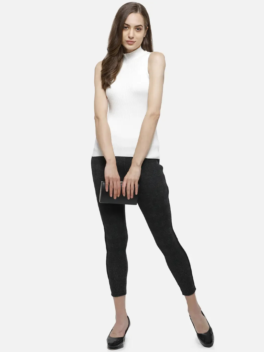 Woman in a 98degreenorth white ribbed high neck sleeveless knit top, black pants, and flats holds a clutch, smiling.