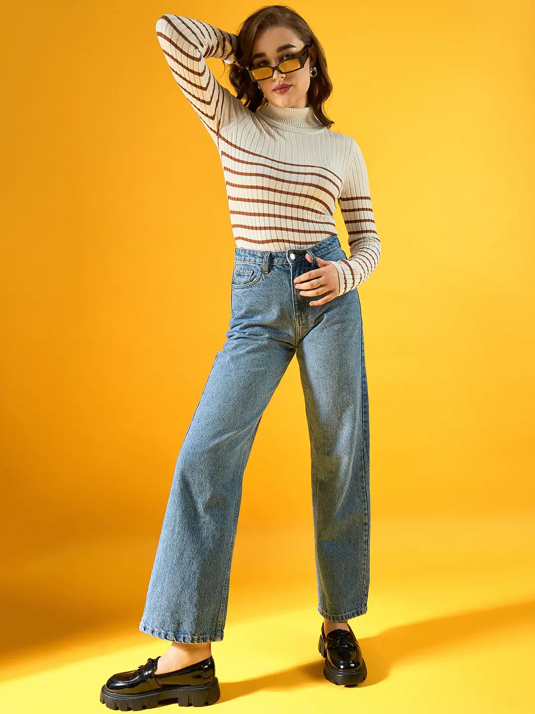 Woman in 98degreenorth white ribbed striped turtleneck sweater poses confidently against a yellow background.
