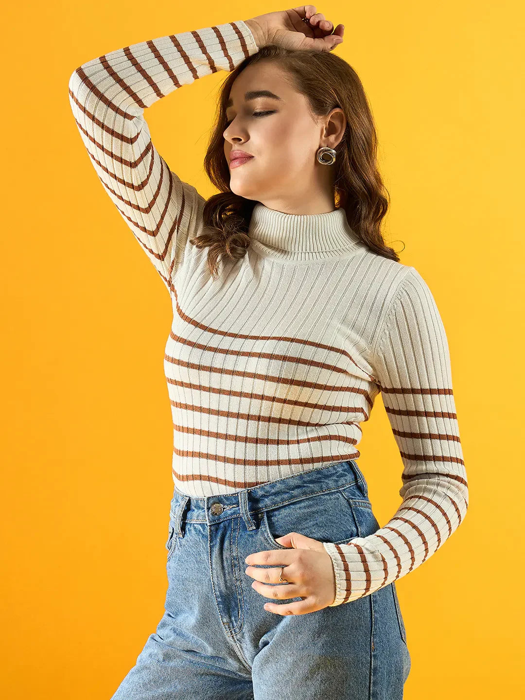 Woman in a 98degreenorth white ribbed striped turtleneck sweater and jeans poses against a yellow background.