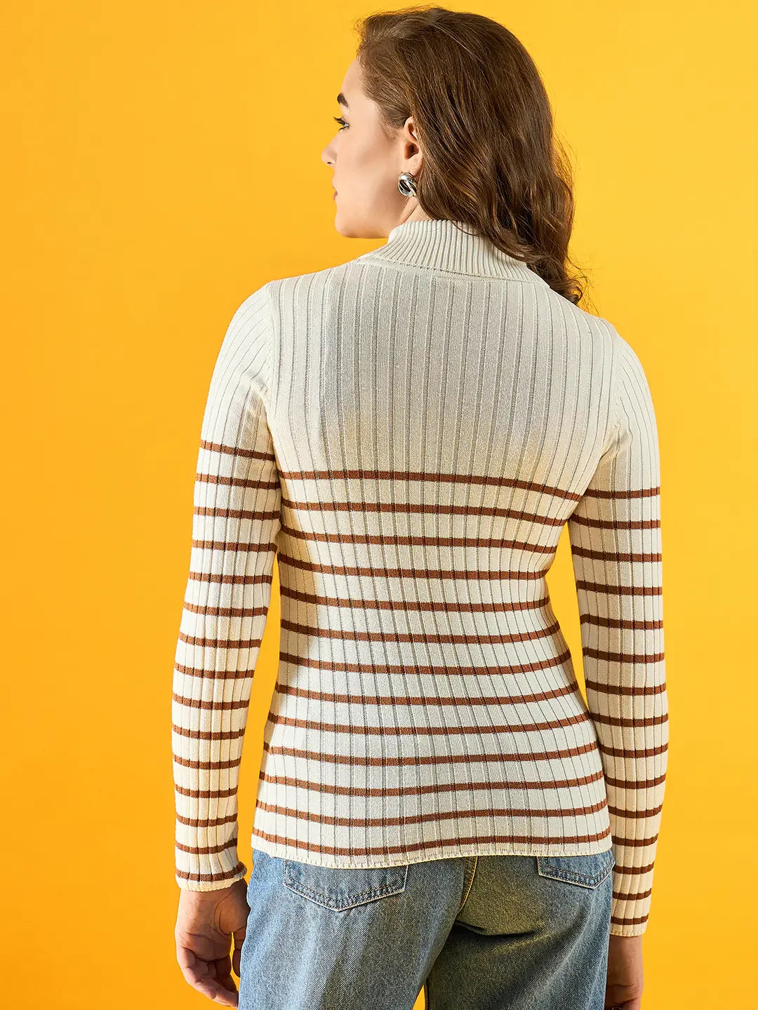 Woman in a 98degreenorth white ribbed striped turtleneck sweater and blue jeans against a yellow background.