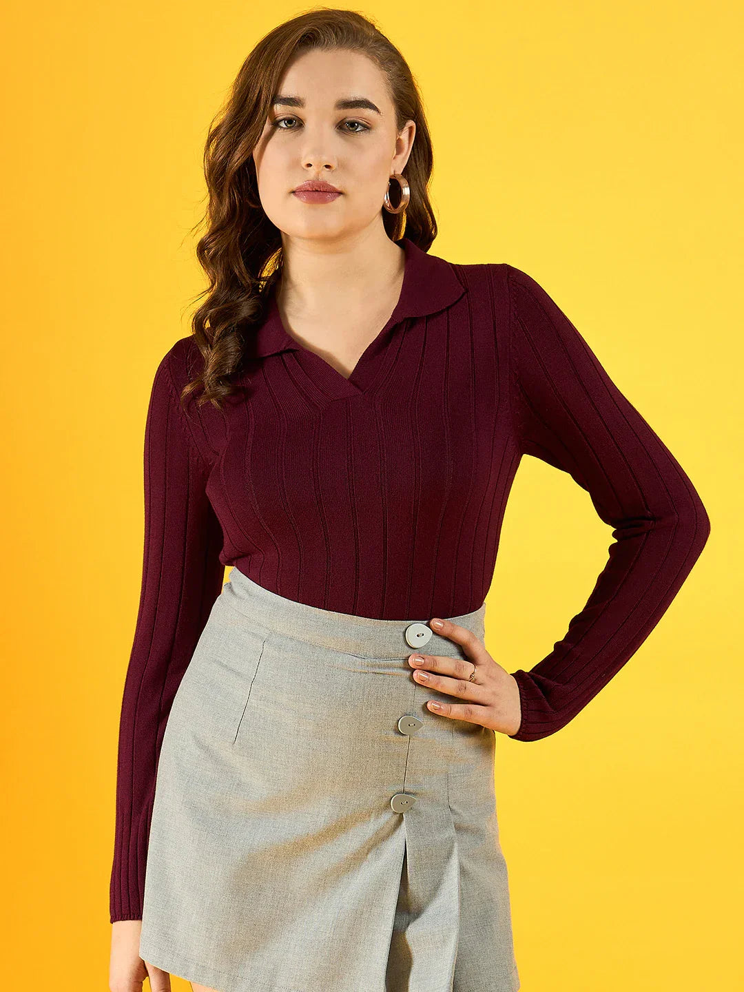 Woman in a 98degreenorth Women’s Wine Ribbed Collar Sweater and gray skirt poses against a yellow background.