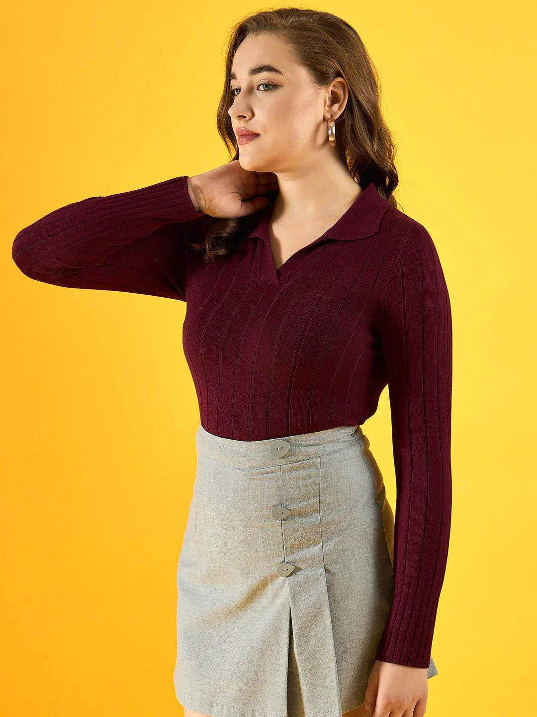 Woman in a 98degreenorth Women’s Wine Ribbed Collar Sweater and light gray skirt stands before a yellow background.
